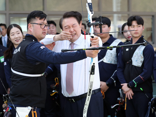 윤석열 대통령이 14일 충북 진천선수촌에서 열린 2023 대한민국 체육비전 보고회를 마친 뒤 양궁장에서 김우진, 최미선 선수가 지켜보는 가운데 화살을 쏘고 있다. 연합뉴스